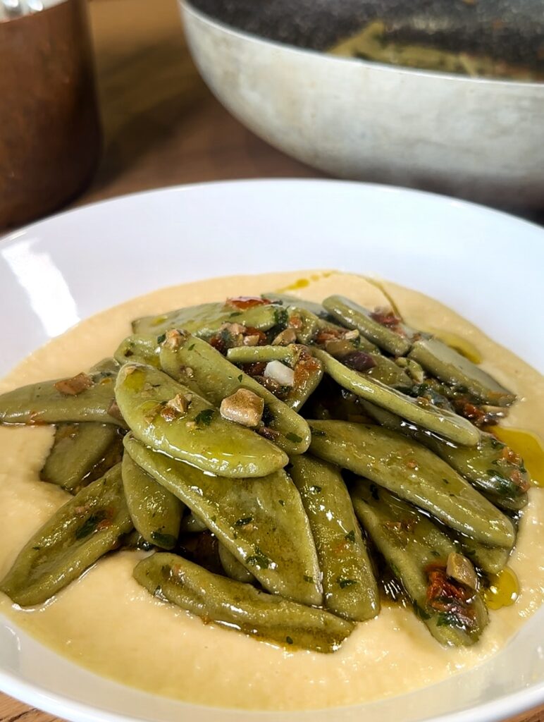 Pasta formato foglie d'olivo con pomodori secchi, capperi e olive, su un letto di humus di ceci